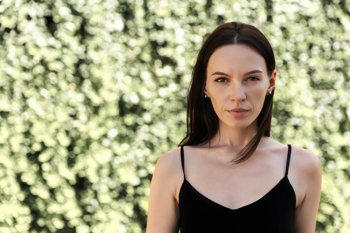 kobieta w wieku około 30 lat z czarnymi włosami w czarnej sukience na ramiączkach stoi na zewnątrz smutna