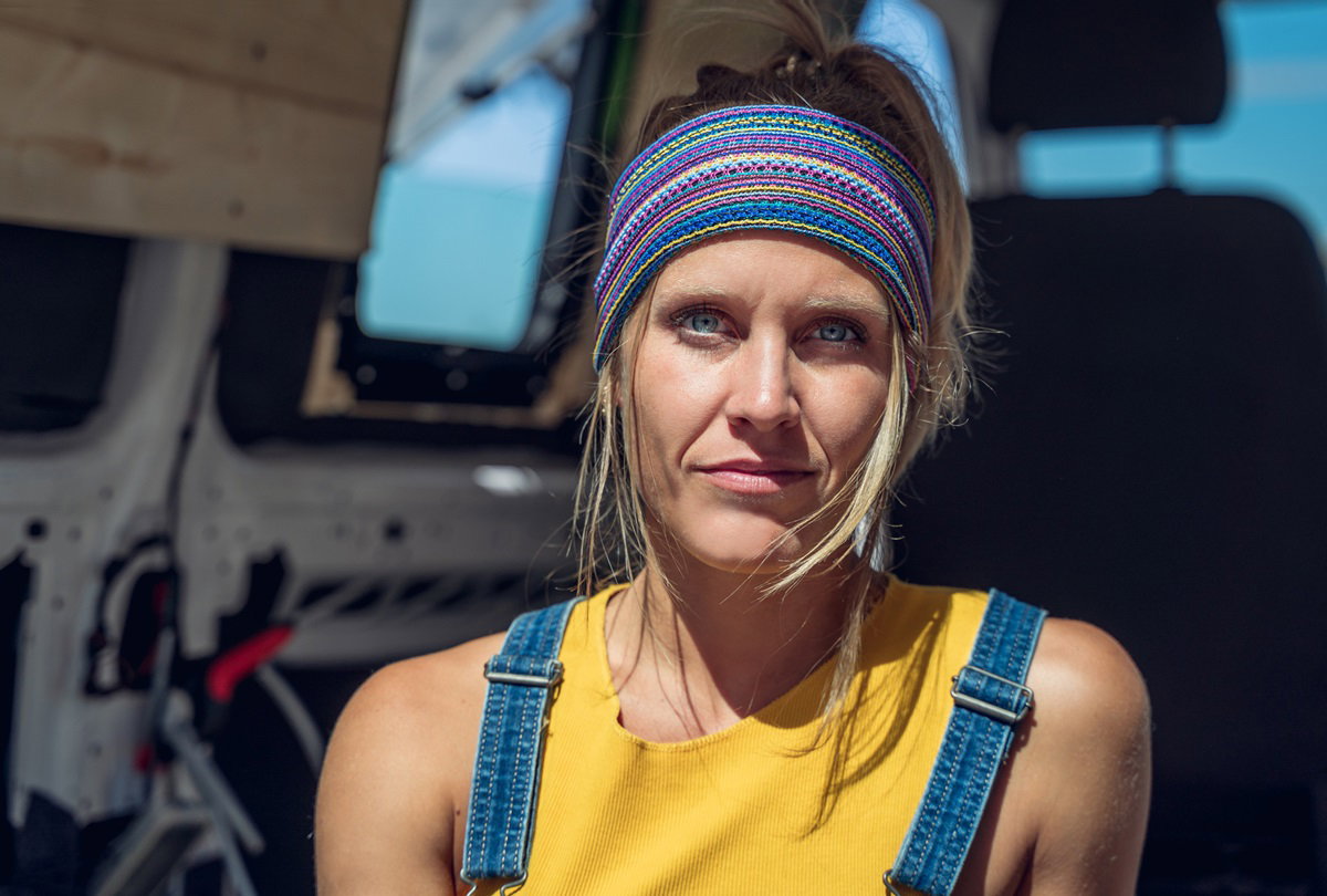 kobieta w wieku około 40 lat z szeroką opaską na głowie i w ogrodniczkach na tle kampera stoi z poważną miną