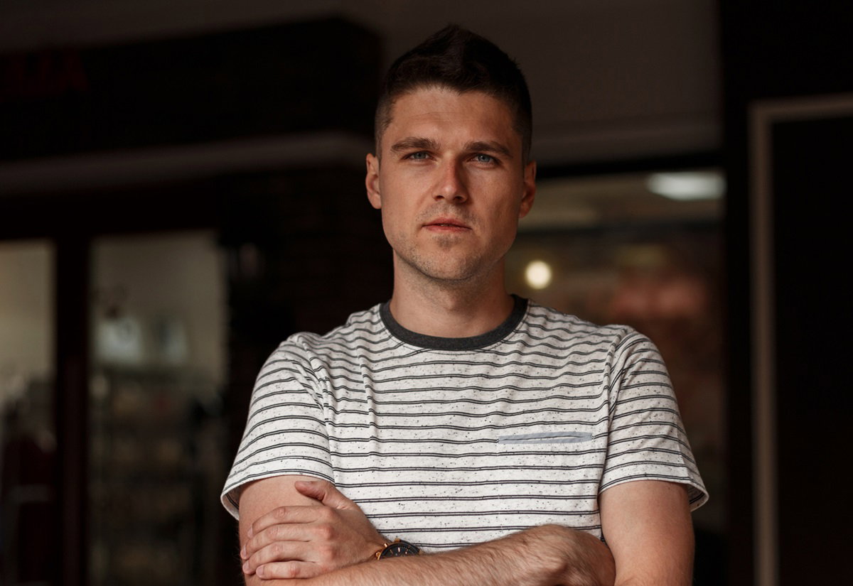 młody mężczyzna w wieku 25 plus w t-shircie w paski stoi w pokoju z założonymi rękami i poważną miną