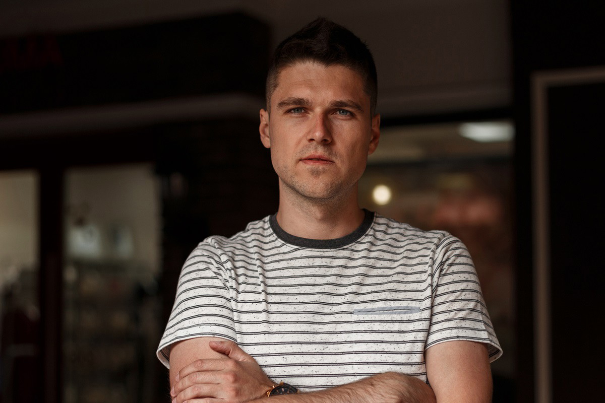młody mężczyzna w wieku 25 plus w t-shircie w paski stoi w pokoju z założonymi rękami i poważną miną