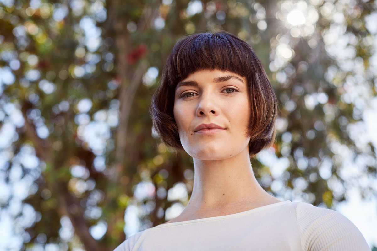 młoda kobieta we fryzurze na pazia z grzywką i białej bluzce stoi na zewnątrz i patrzy z wyższością