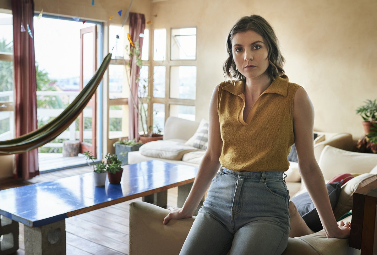 kobieta w wieku około 30 lat siedzi w domu w jeansach i dzianinowej bluzce opiera się o kanapę i ma poważną minę