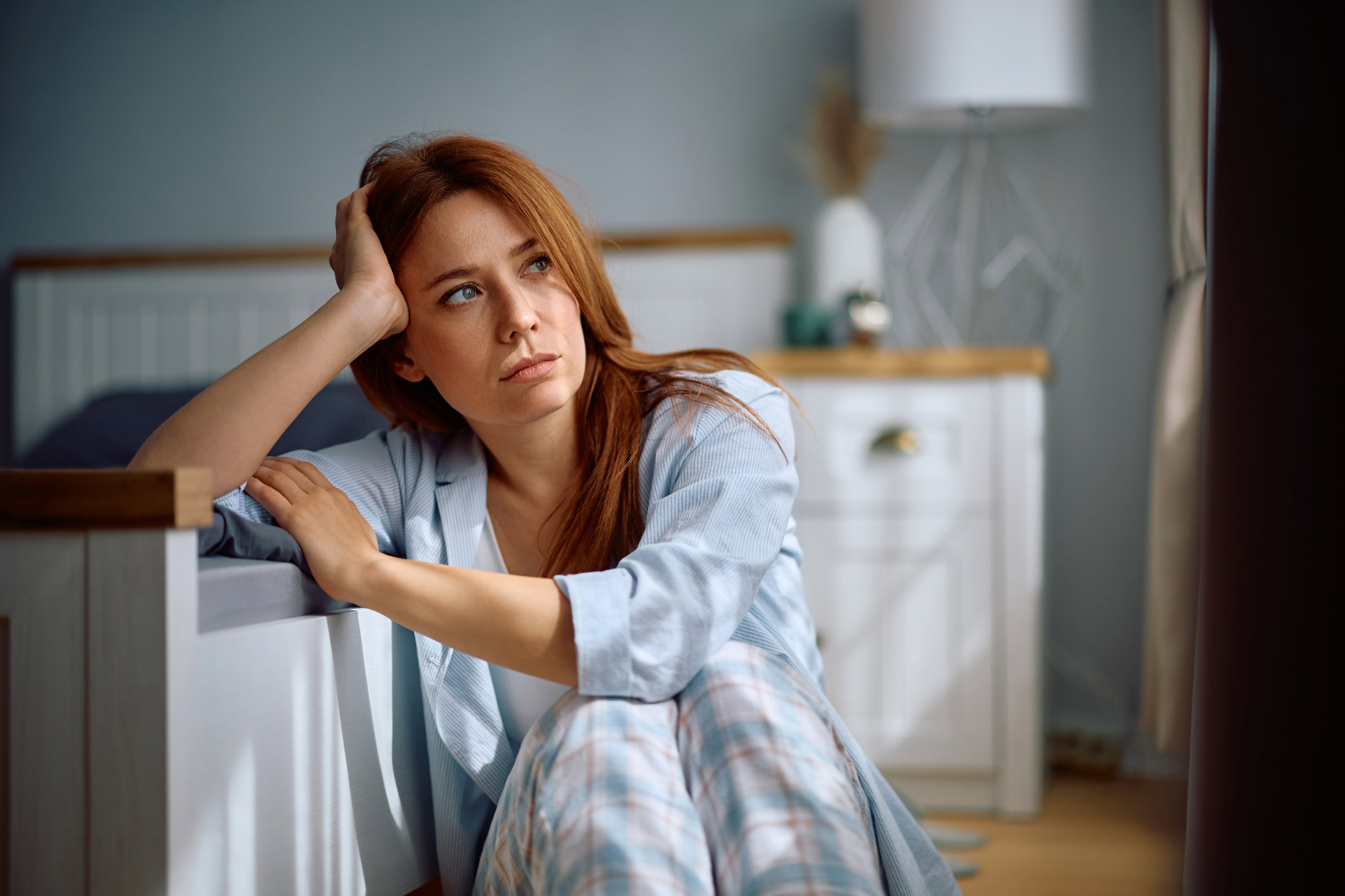 Depressed woman sitting on the floor in bedroom in the morning.