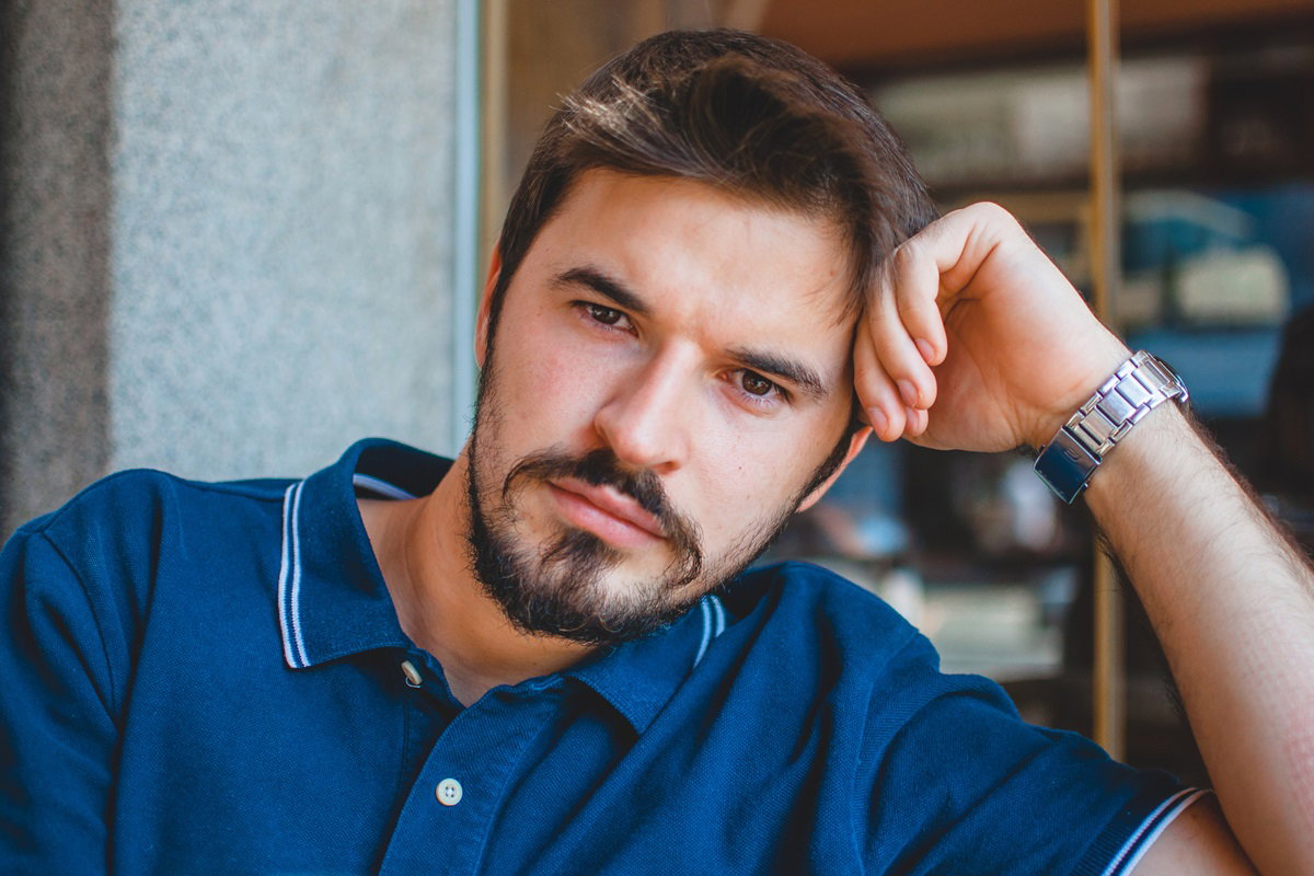 młody mężczyzna w wieku około 30 lat z zarostem w niebieskim polo siedzi zamyślony