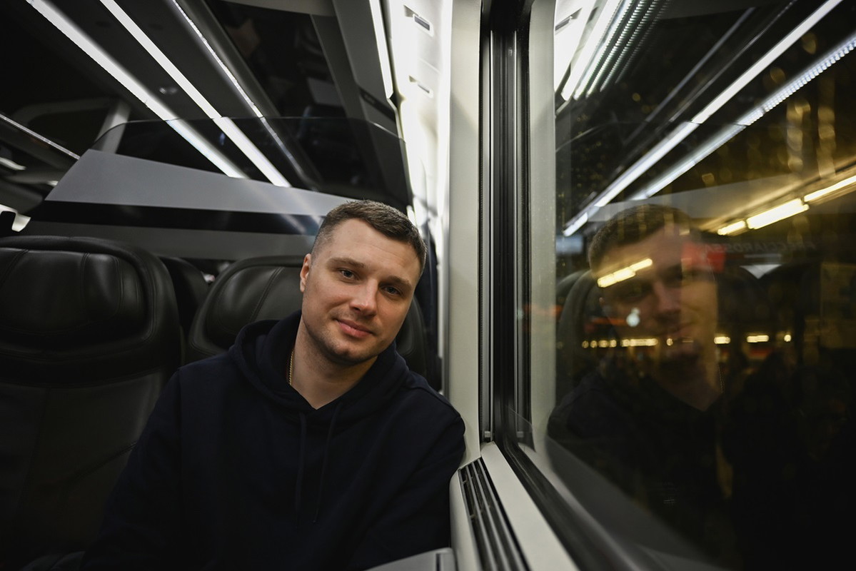 młody mężczyzna siedzi w pociągu przy oknie i lekko się uśmiecha zamyślony