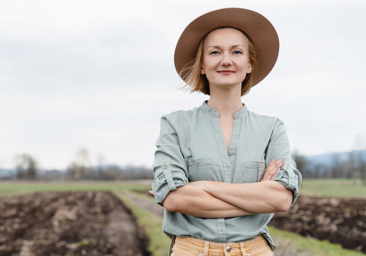 kobieta w wieku 35 plus w kapeluszu stoi na tle pola z zadowolona mina