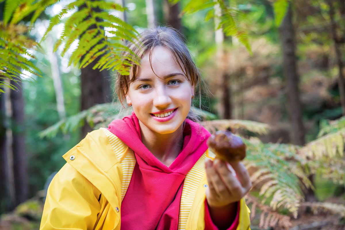młoda dziewczyna w żółtej kurtce na grzybobraniu z grzybem w ręce uśmiechnięta