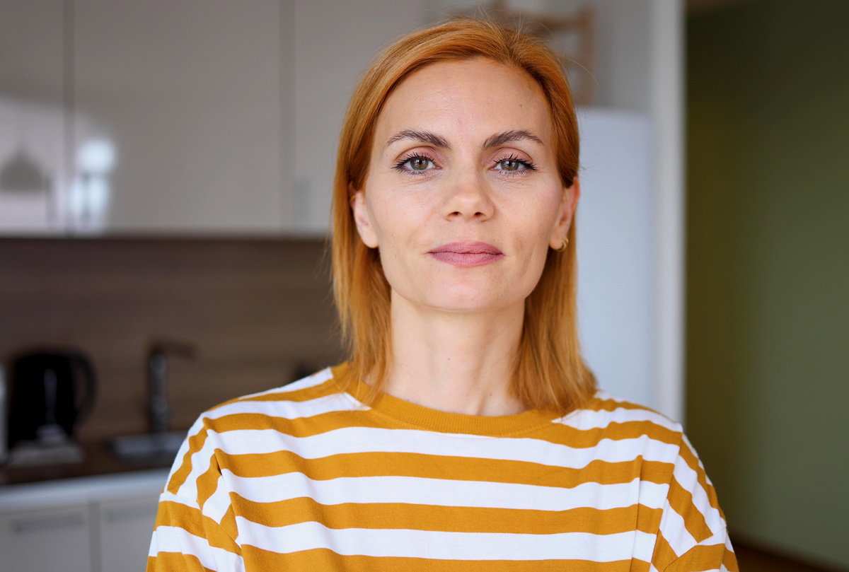 młoda kobieta z jasnopomarańczowymi włosami w pasiastym t-shircie stoi w kuchni i ma kpiącą minę