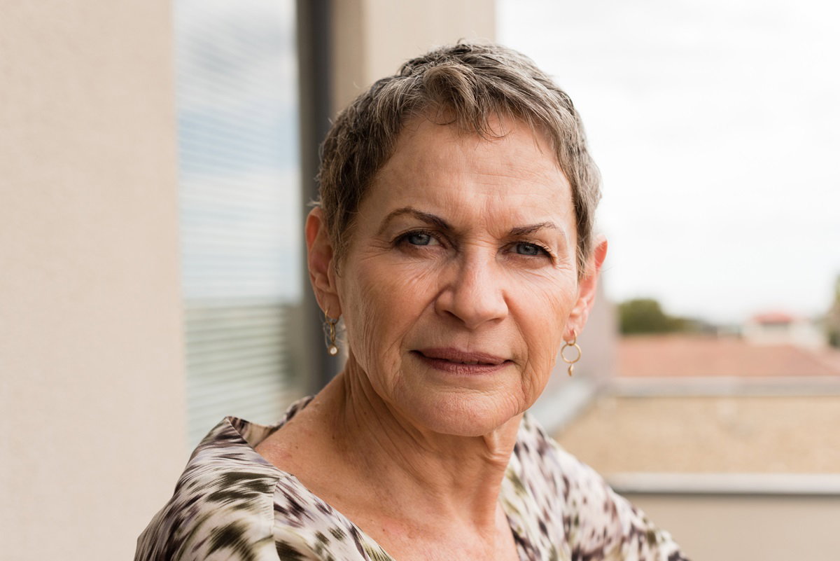 kobieta w wieku około 65+ z krótkimi włosami we wzorzystej sukience siedzi na balkonie z zaciętą miną