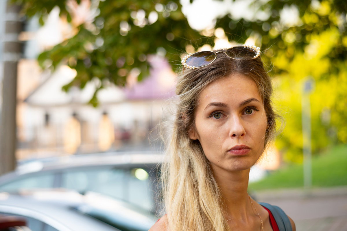 młoda kobieta blondynka z długimi włosami i z okularami na głowie stoi na zewnątrz ze smutną miną