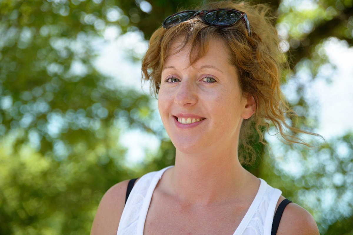 kobieta w wieku 30 plus z okularami na głowie i w topie stoi na zewnątrz i uśmiecha się