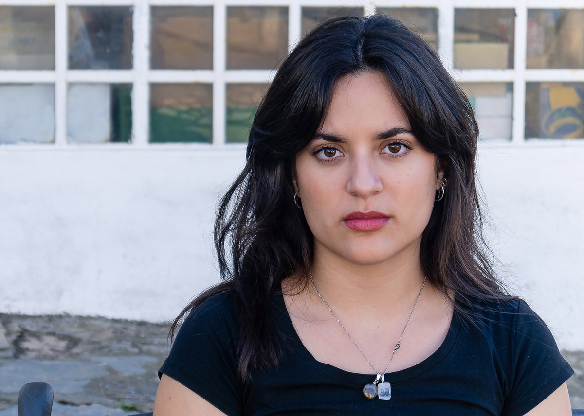 młoda kobieta z ciemnymi włosami siedzi na przystanku ze smutnym spojrzeniem