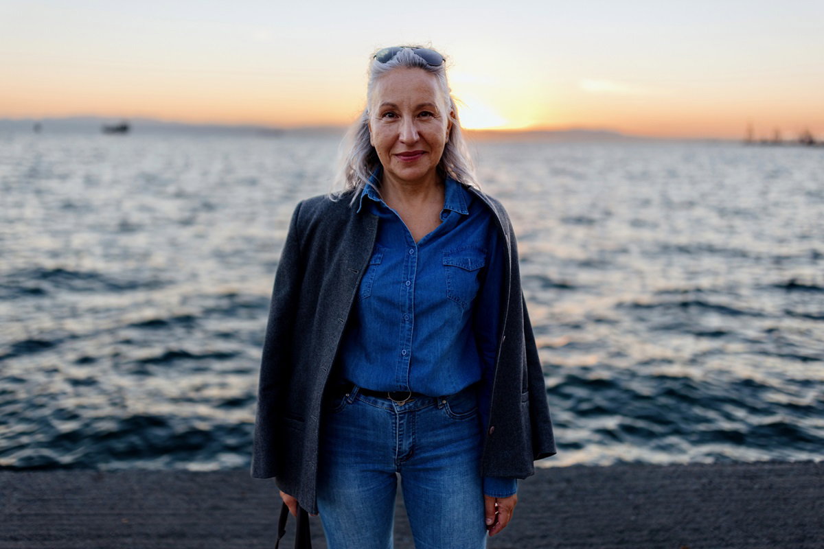 kobieta w wieku około 60 lat stoi na tle morza i lekko się uśmiecha