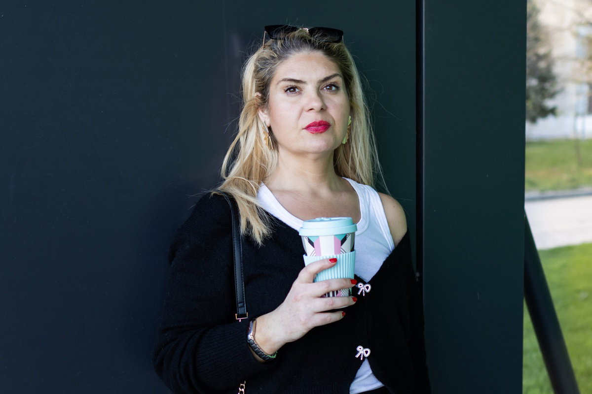 kobieta w wieku około 45 plus blondynka stoi na klatce schodowej na tle drzwi z kubkiem kawy w ręce i zamyśloną miną