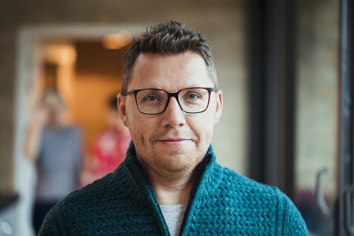 mężczyzna w średnim wieku w okularach i rozpinanym swetrze stoi w salonie i uśmiecha się zadowolony