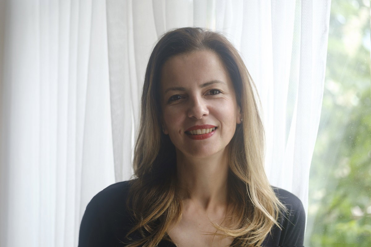 kobieta w wieku 35 plus z długimi włosami stoi na tle okna i uśmiecha się rozmarzona