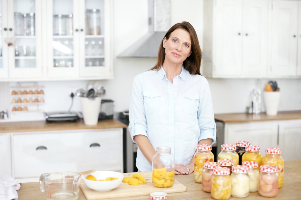 młoda kobieta stoi w kuchni i robi przetwory z brzoskwiń i innych owoców