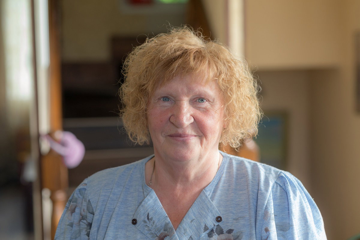 kobieta w wieku około 60 plus stoi na tle schodów i uśmiecha się zawadiacko