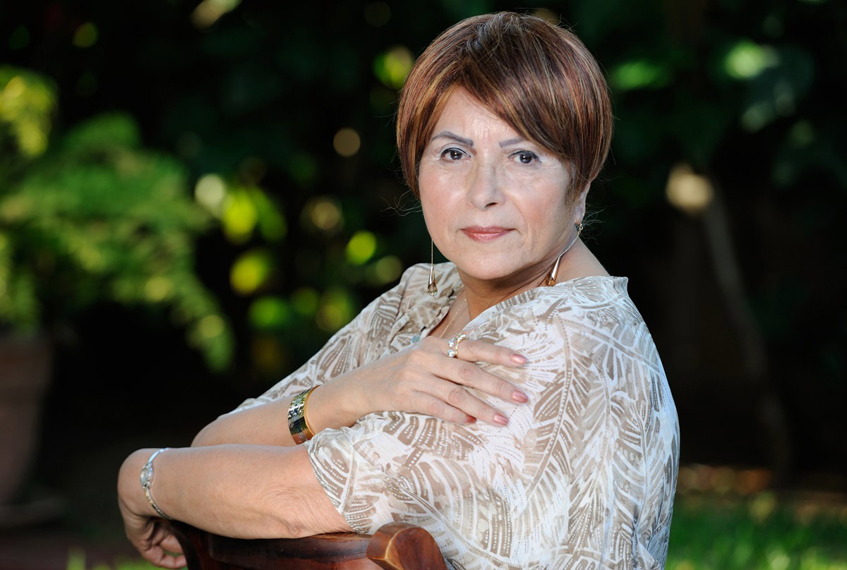 dojrzała kobieta w wieku około 60 lat siedzi na zewnątrz na tle roślinności z zamyśloną miną