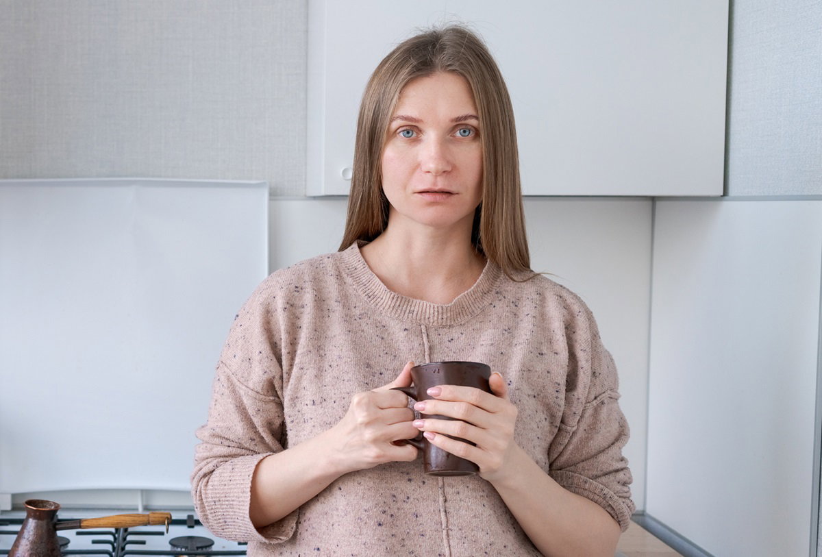 młoda kobieta stoi w kuchni z kubkiem w ręce i jest bardzo smutna
