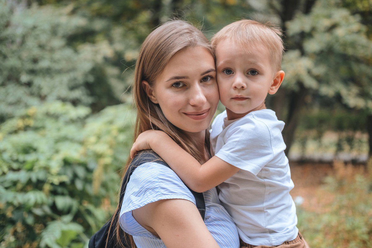 młoda mama stoi w parku i ma na rękach synka w wieku około 3 lat