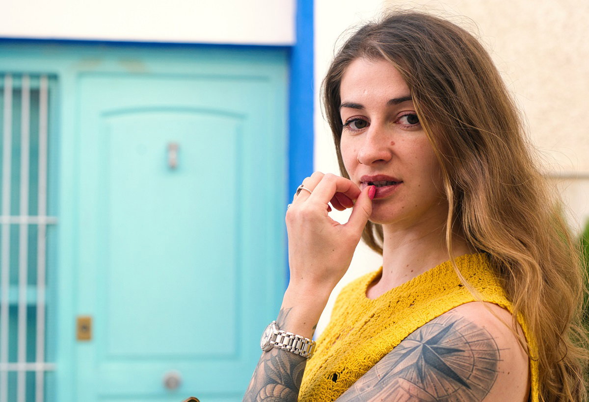 kobieta z długimi włosami i w dzianinowej bluzce siedzi zamyślona na tle niebieskich drzwi