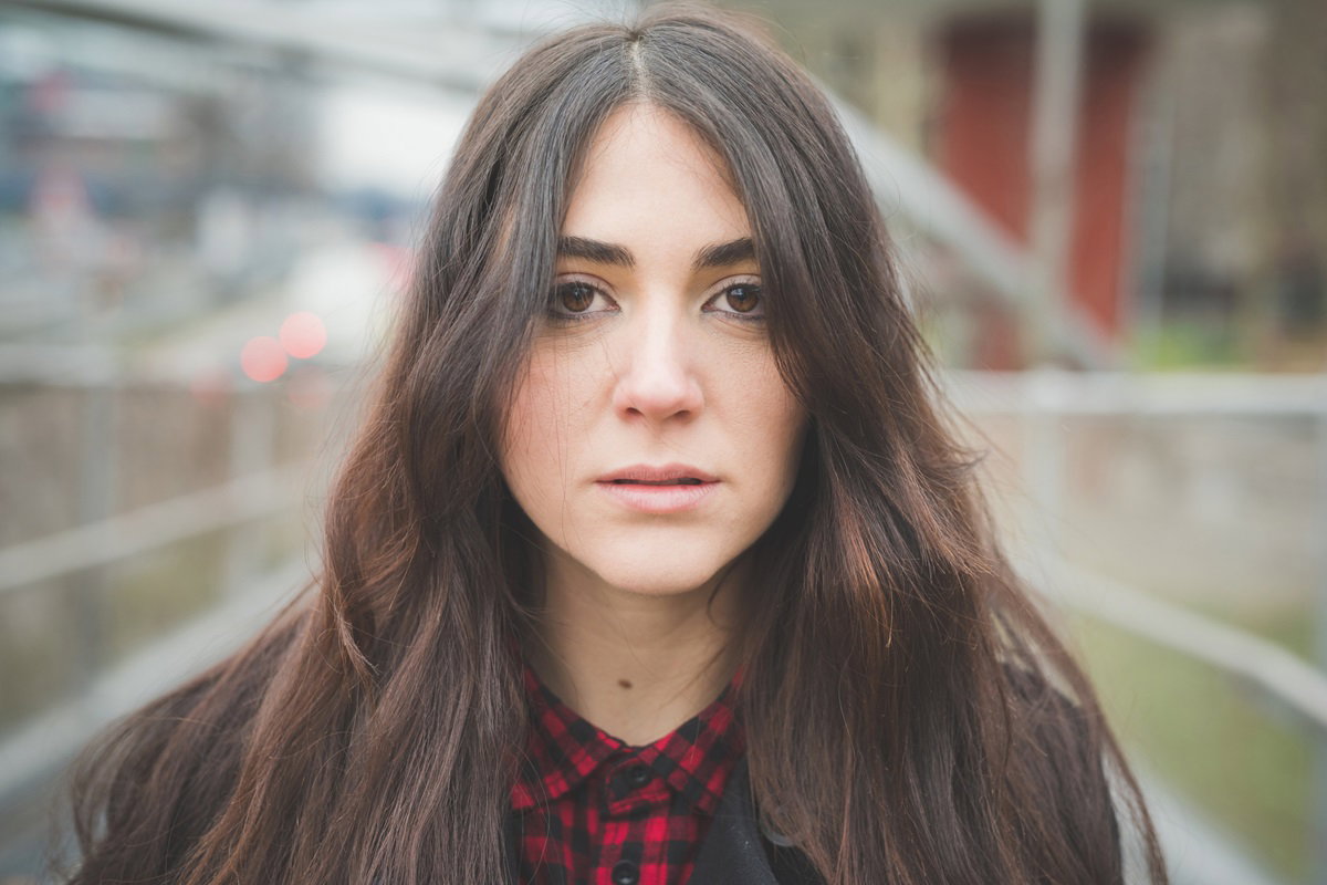 młoda kobieta z ciemnymi długimi włosami stoi na zewnątrz ze zrozpaczoną miną