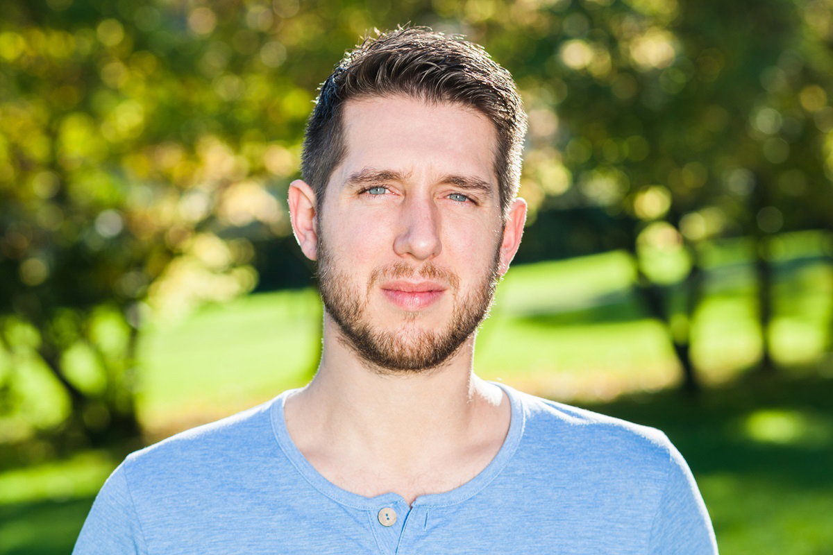 młody mężczyzna w wieku około 30 lat w niebieskiej bluzce z zarostem stoi na zewnątrz ze smutną miną