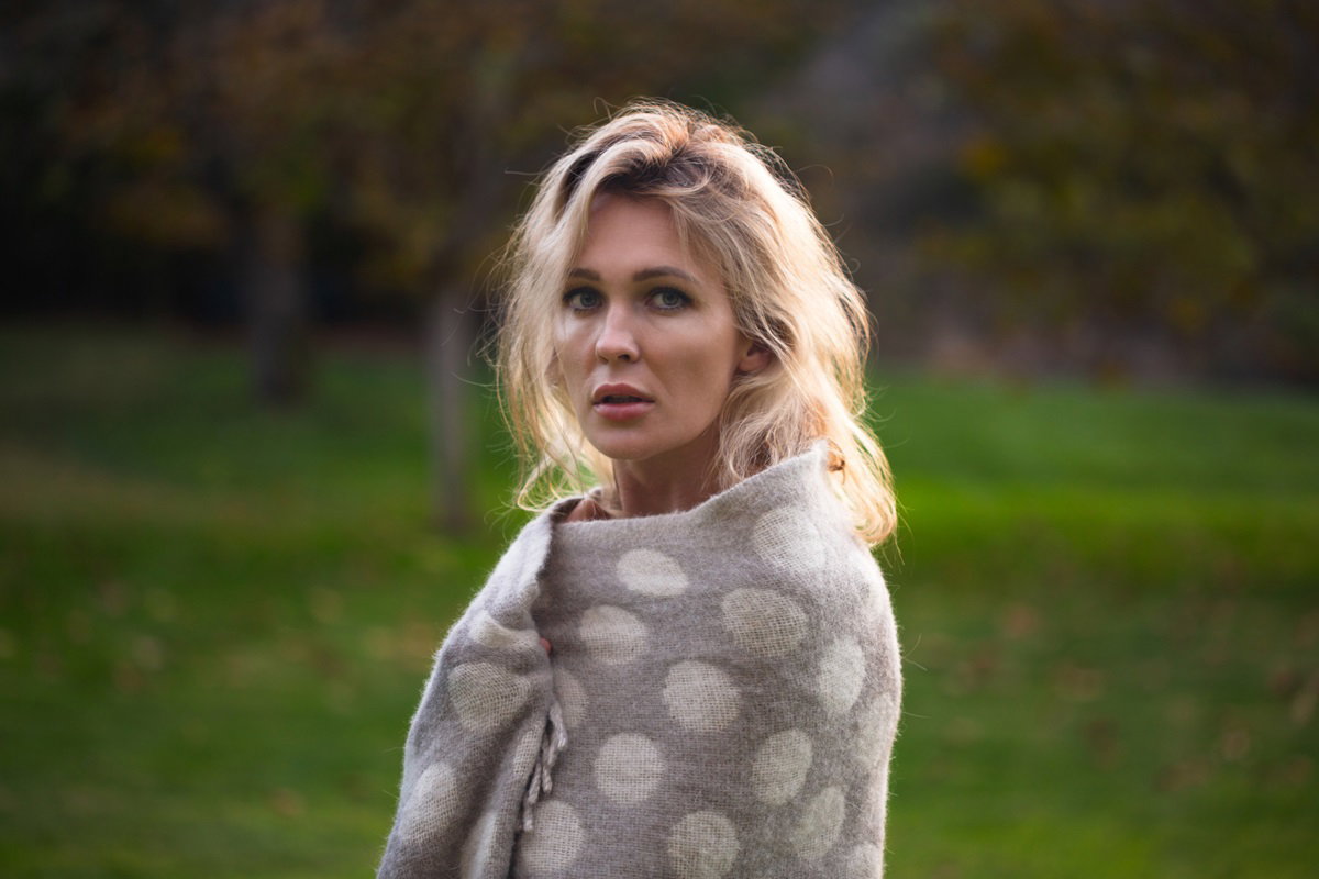 młoda kobieta blondynka stoi a zewnątrz owinięta kocem w wielkie grochy ze smutną miną