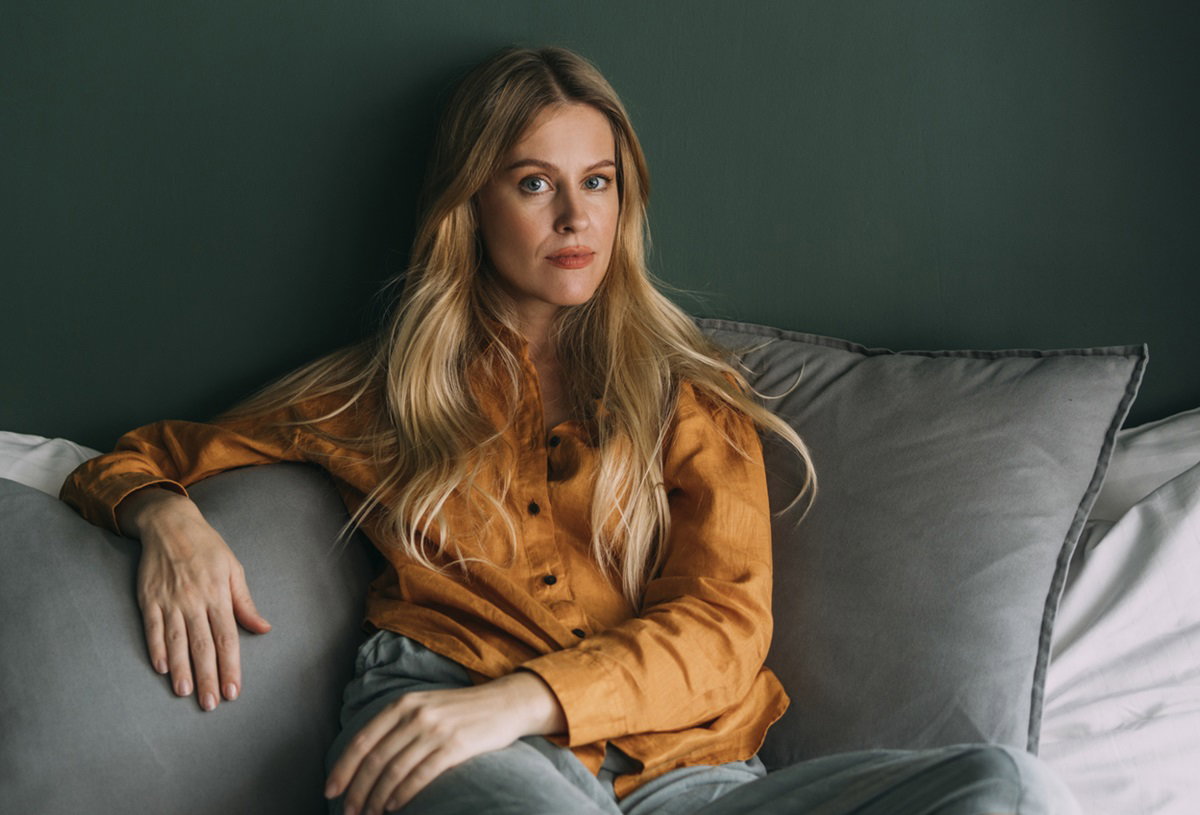 kobieta w wieku 35 plus blondynka z długimi włosami siedzi na kanapie i ma zawiedzione spojrzenie
