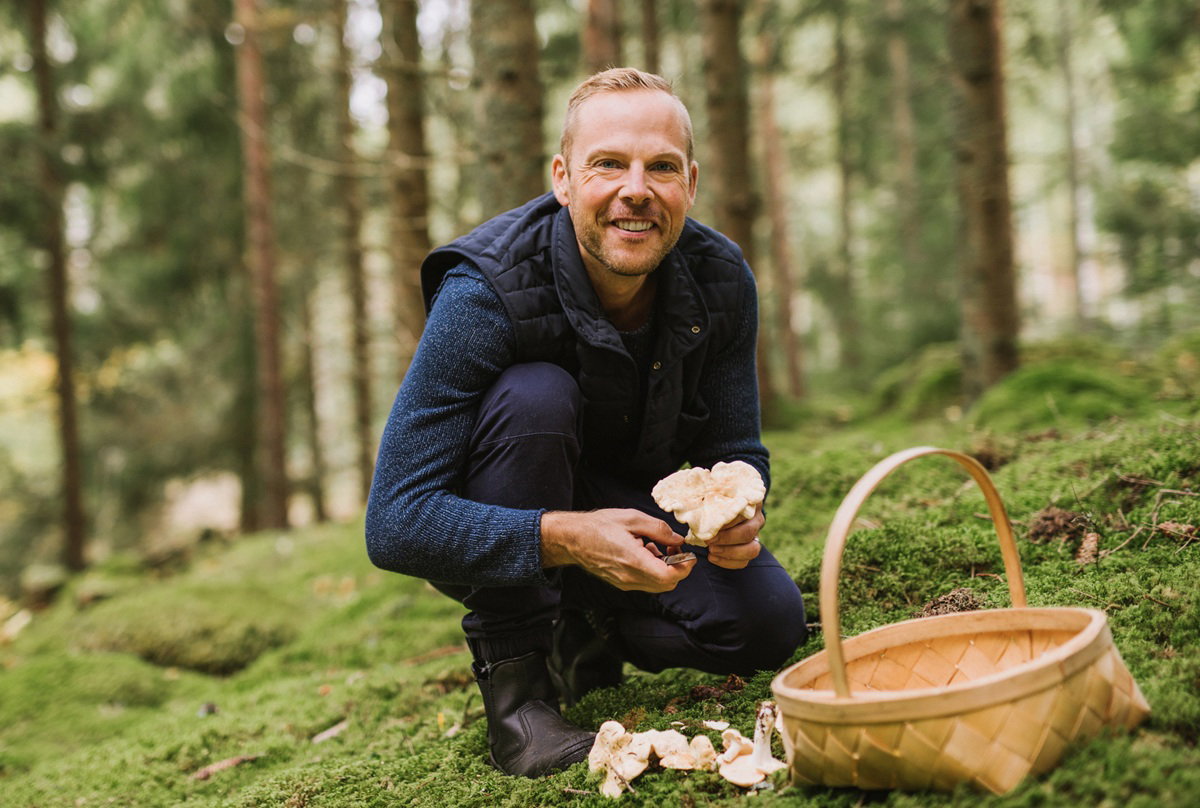 mężczyzna w wieku 35 lat na grzybobraniu uśmiecha się nad koszykiem i grzybami