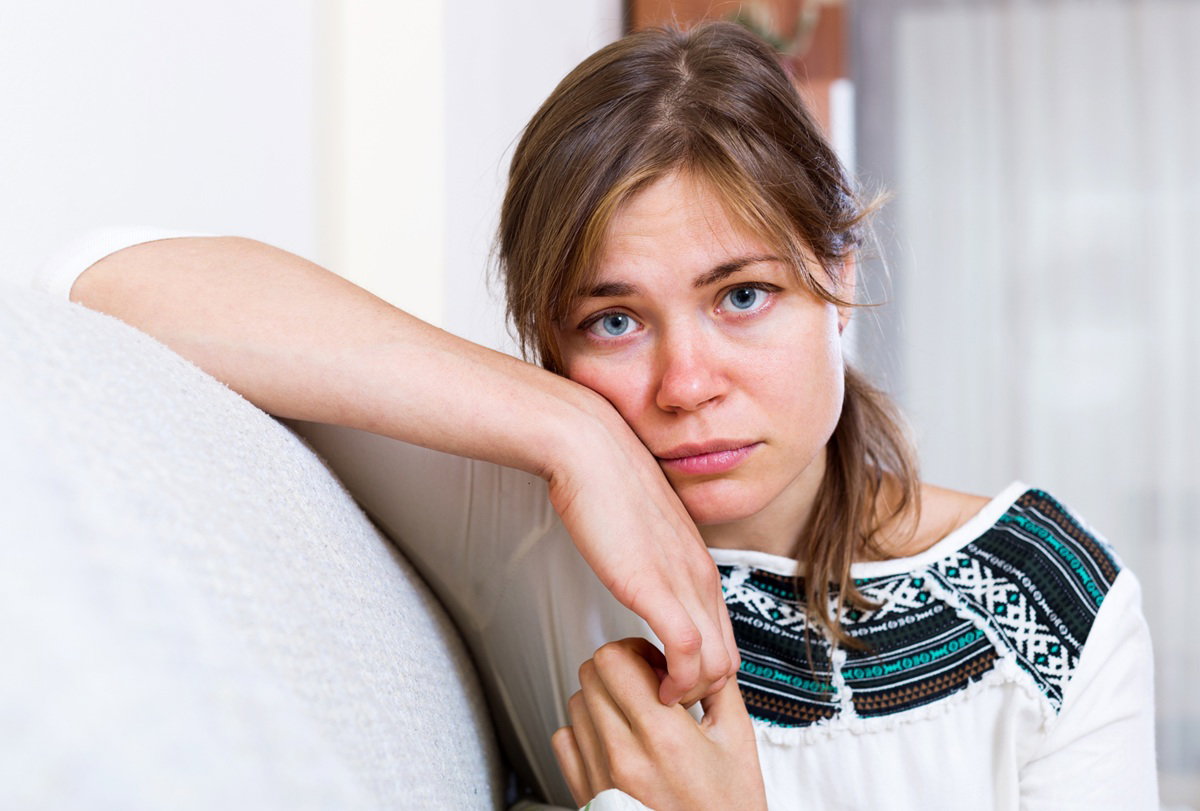 młoda kobieta 25 plus w bluzce z haftem siedzi zmartwiona na kanapie