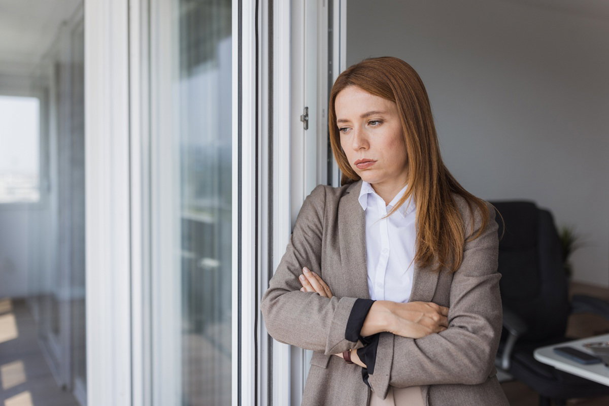 kobieta w wieku około 30 plus w marynarce i koszuli stoi przy oknie i oddycha z ulgą