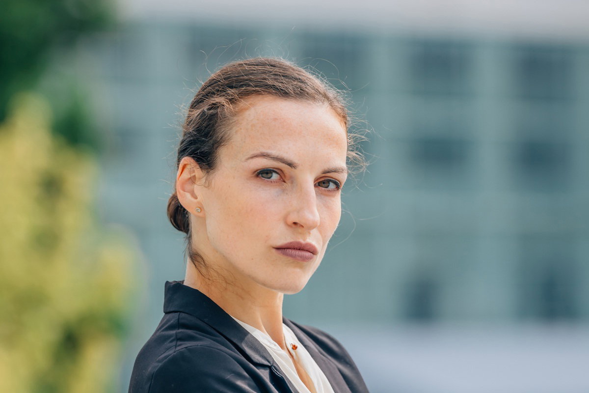 młoda kobieta około 35 plus stoi na tle budynku z surowym spojrzeniem