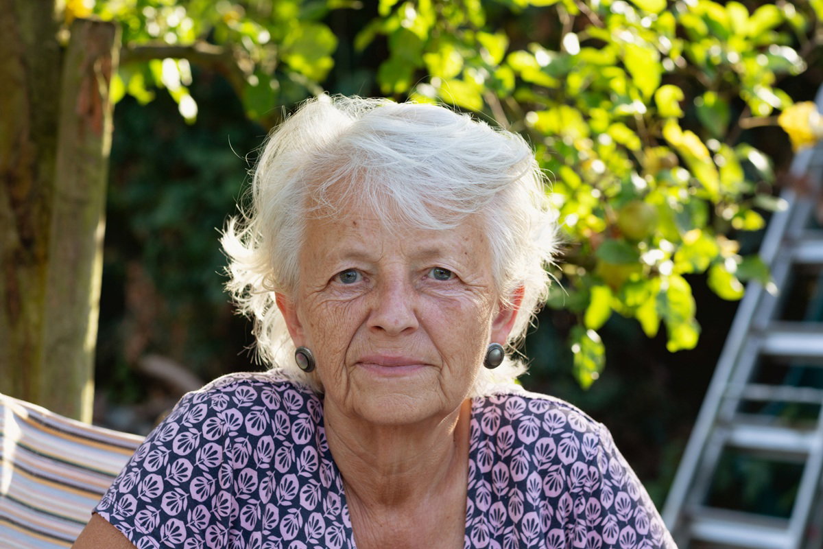 kobieta w wieku 65 plus z siwymi włosami siedzi na zewnątrz i lekko się uśmiecha