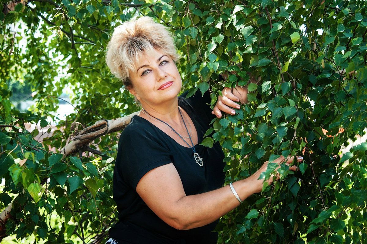 kobieta 55 plus blondynka stoi na tle brzóz zamyślona