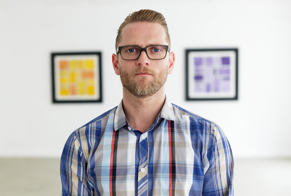 mężczyzna w wieku 35 lat plus w kraciastej koszuli i okularach stoi na tle graficznych obrazków