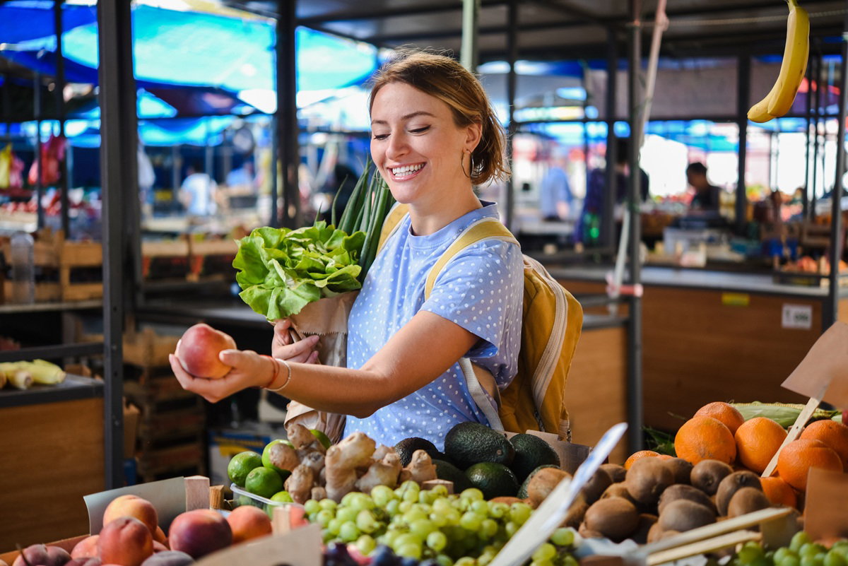 młoda kobieta z uśmiechem wybiera brzoskwinie na targu