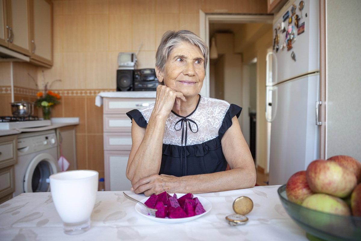 kobieta w wieku 60 plus z krótkimi siwymi włosami siedzi w kuchni przy stole z talerzykiem buraków