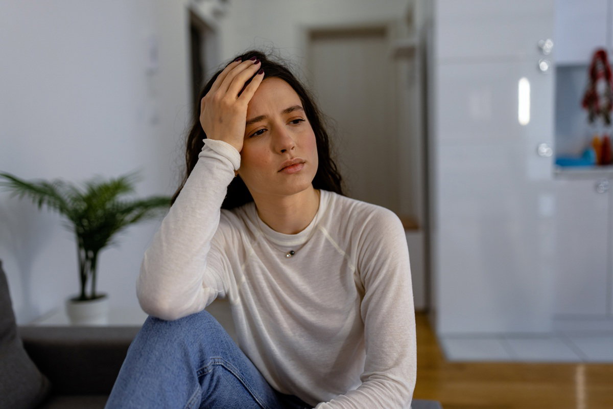 młoda kobieta w wieku około 25 plus z ciemnymi długimi włosami siedzi zmartwiona w salonie