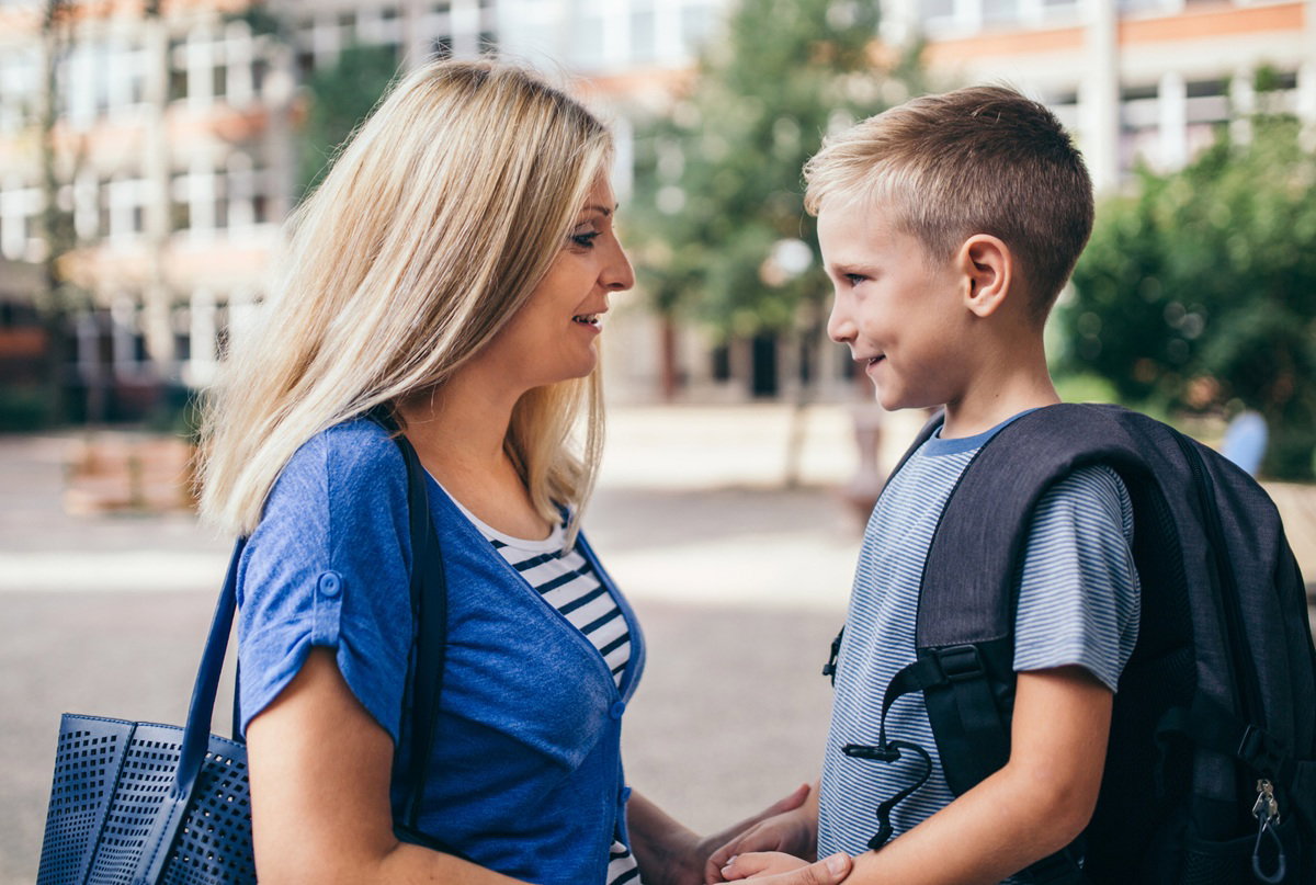 mama blondynka z synkiem stoi przed szkołą 1 września