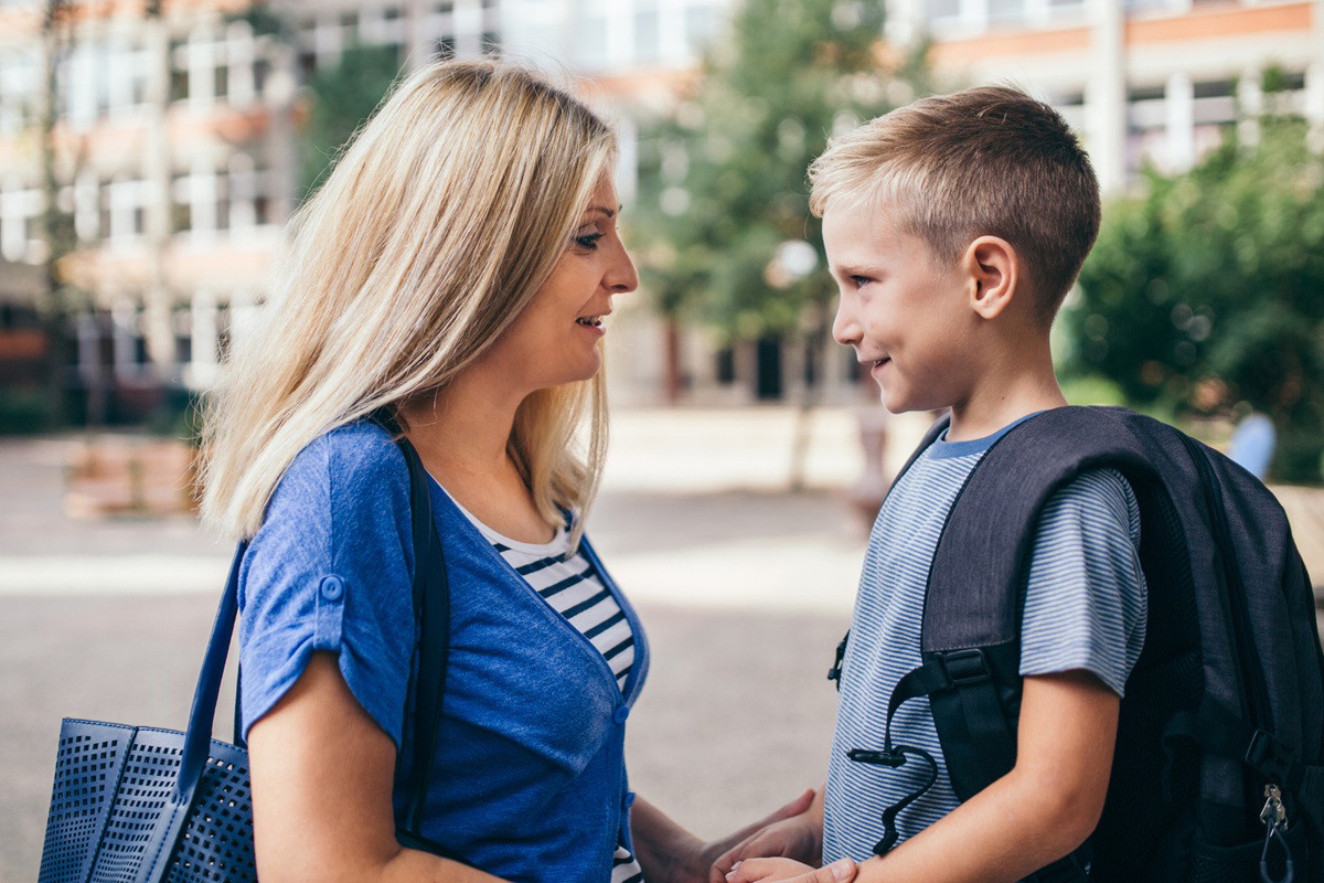 mama blondynka z synkiem stoi przed szkołą 1 września
