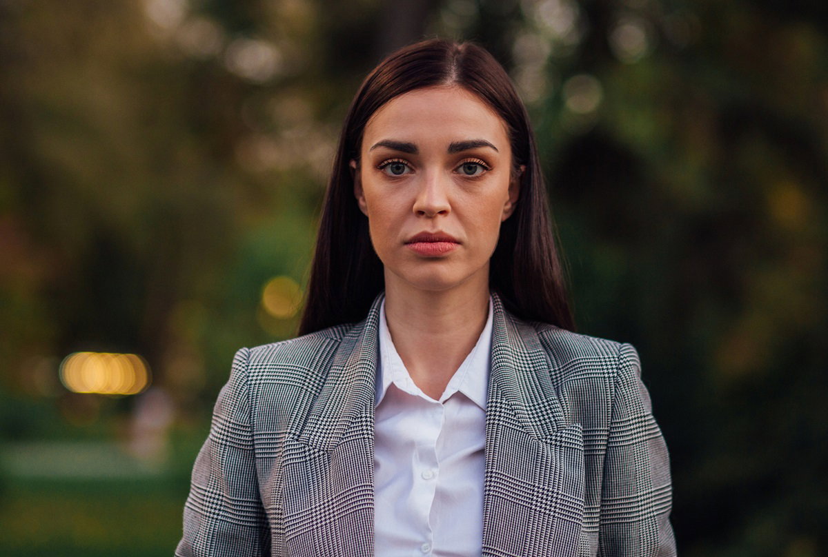 młoda kobieta z długimi włosami w marynarce w drobną kratkę stoi smutna na zewnątrz