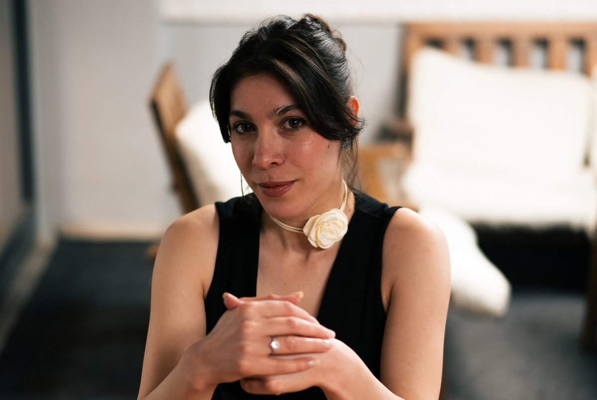 młoda dziewczyna w wieku 25 plus w czarnym topie i z różą na szyi siedzi zamyślona w pokoju