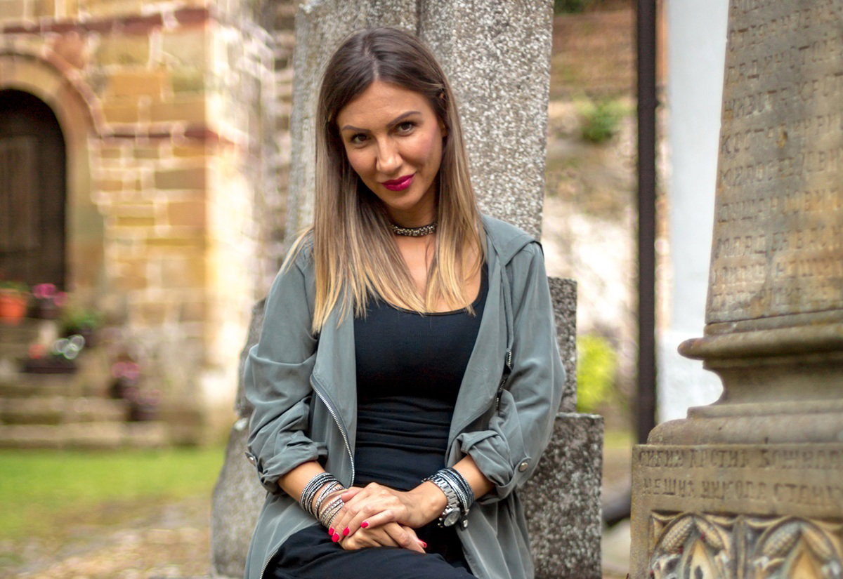 kobieta w wieku 35 plus blondynka siedzi na tle kościoła z prowokacyjnym uśmiechem