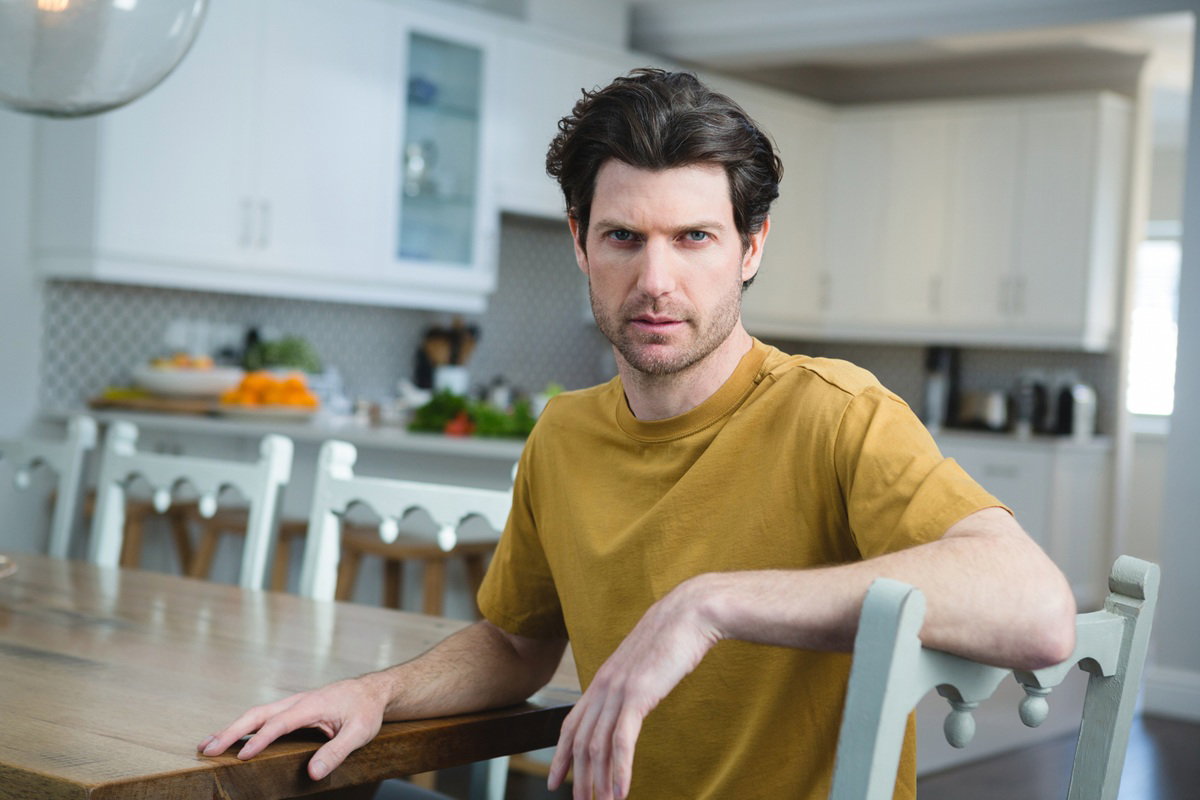 młody mężczyzna w wieku 35 plus w musztardowej koszulce patrzy przed siebie rozgoryczony