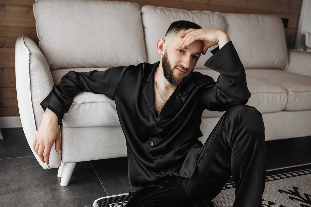 młody mężczyzna z brodą ubrany na czarno siedzi na podłodzie zmartwiony
