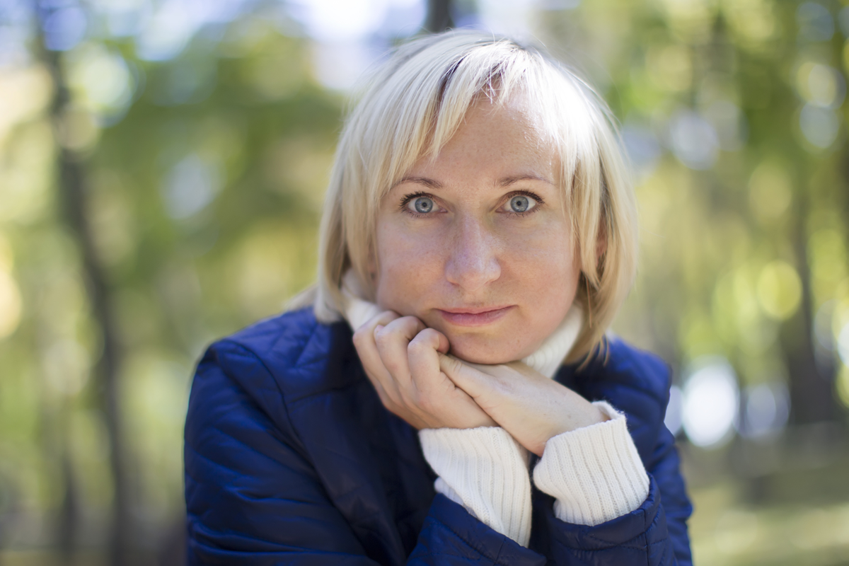 kobieta w wieku około 35 lat blondynka w granatowej kurtce siedzi na zewnątrz nieco wystraszona
