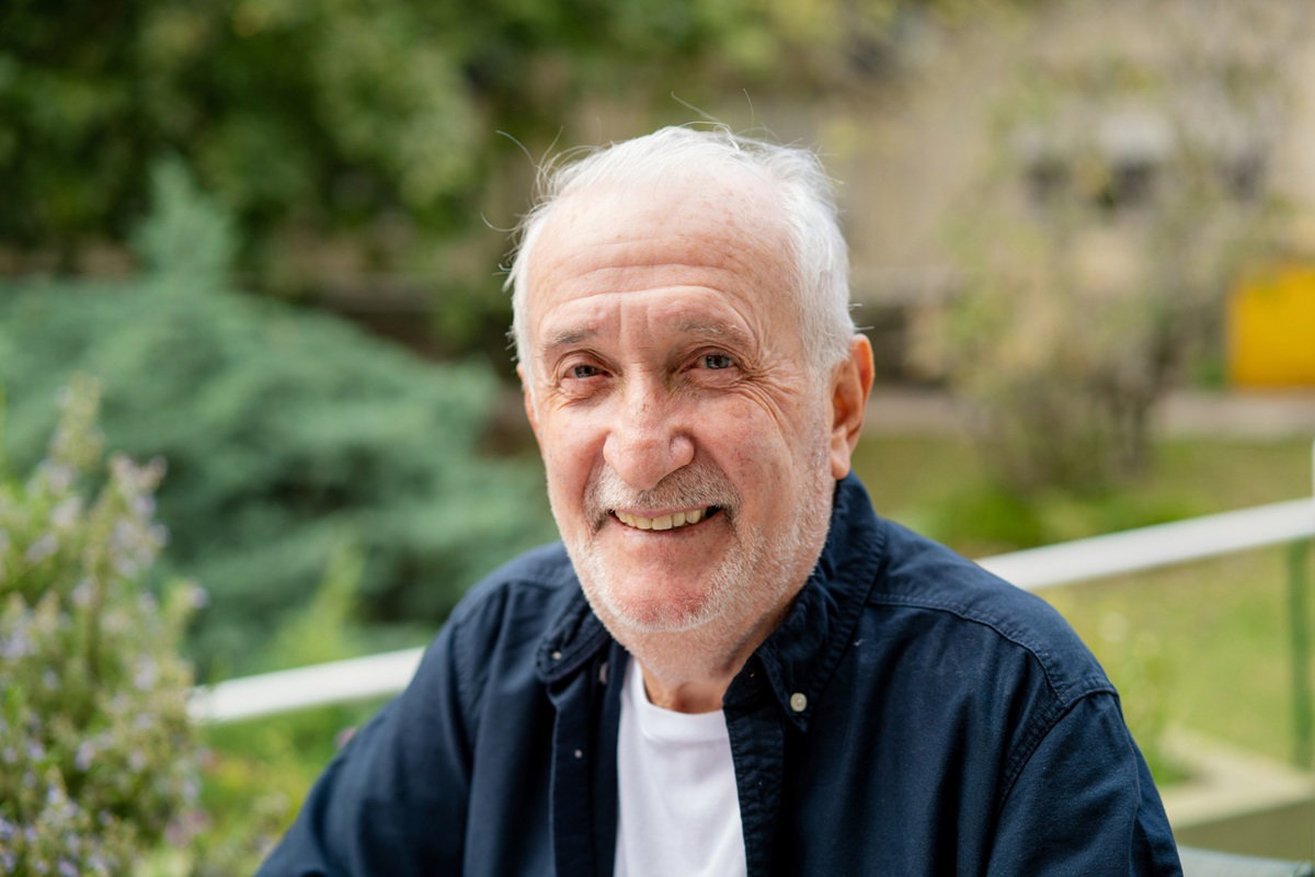 mężczyzna w wieku 75 plus siwy łysiejący siedzi na zewnątrz i się uśmiecha