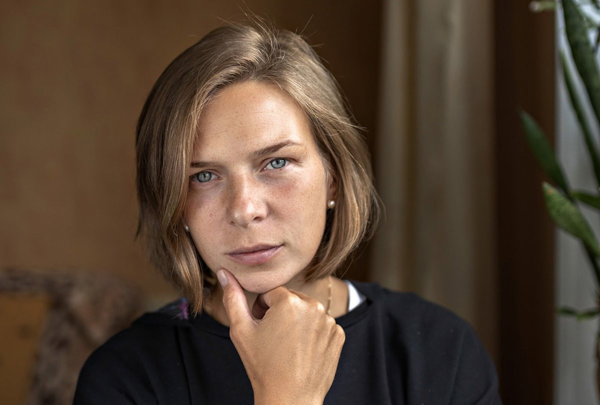 młoda kobieta we fryzurze typu paź i ciemnych włosach blond siedzi zamyślona i smutna w ciemnym salonie